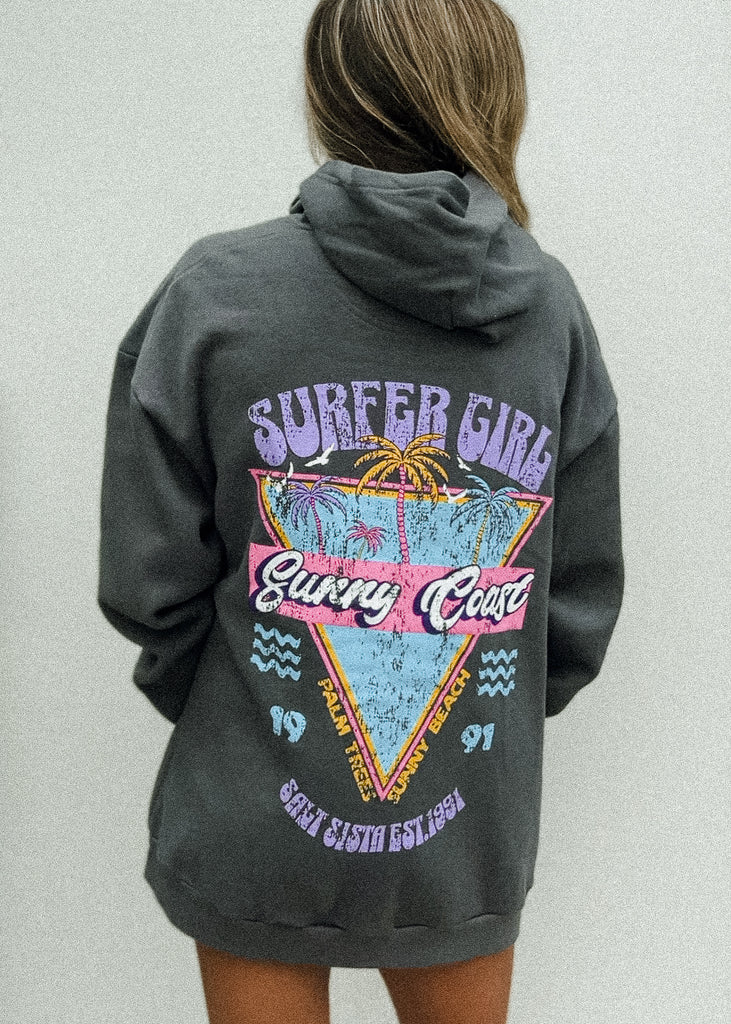 Person wearing a dark gray hoodie with a colorful 'Surfer Girl' design on the back against a light gray background