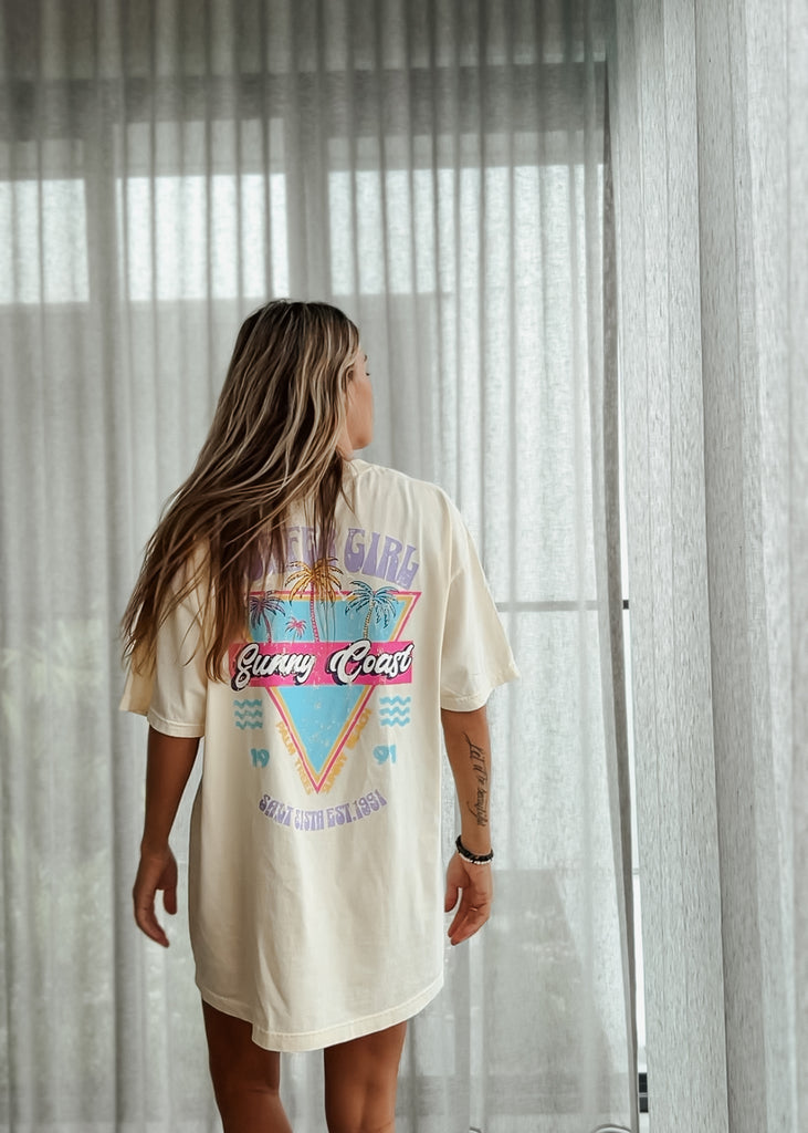 Person wearing a graphic t-shirt with a colorful design, standing in front of sheer curtains.