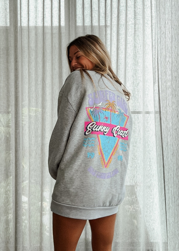 Person wearing a gray sweatshirt with a colorful graphic design on the back, standing against a light curtain background.
