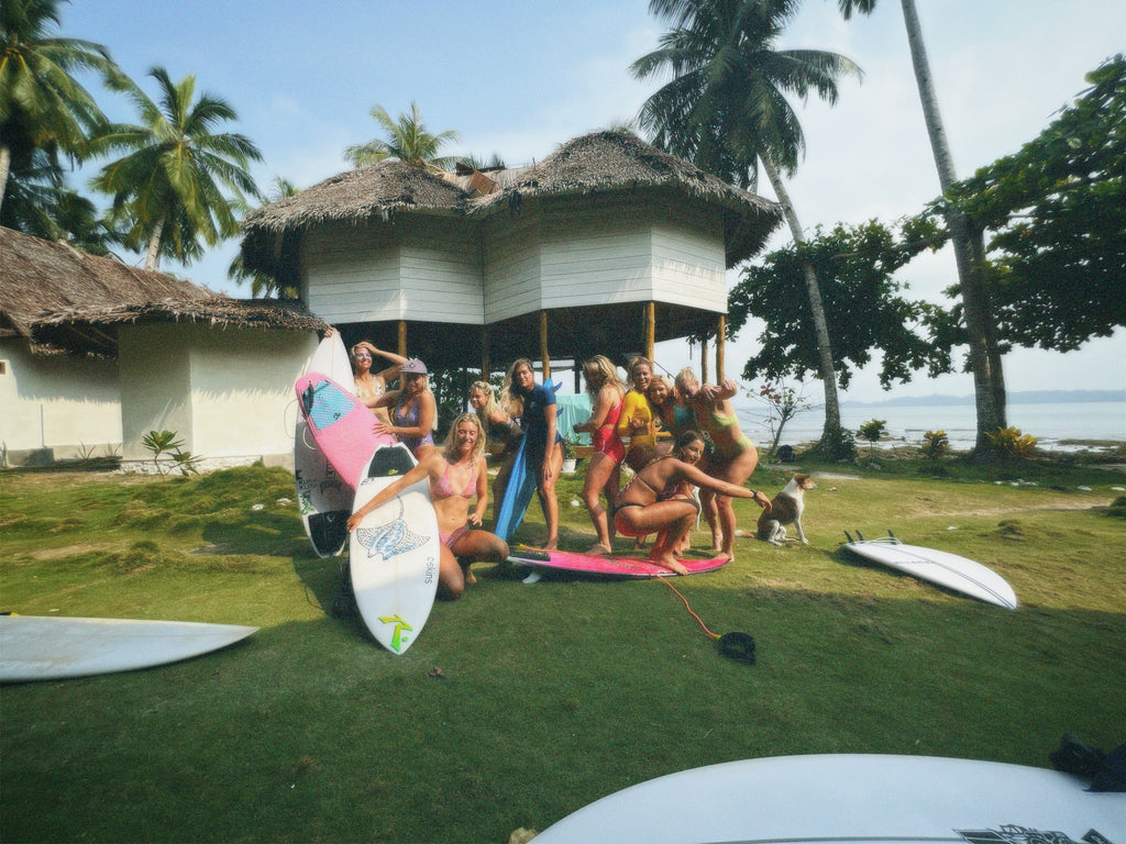 Group of people with surfboards near thatched-roof huts on a tropical beach in the Mentawai Islands Indonesia